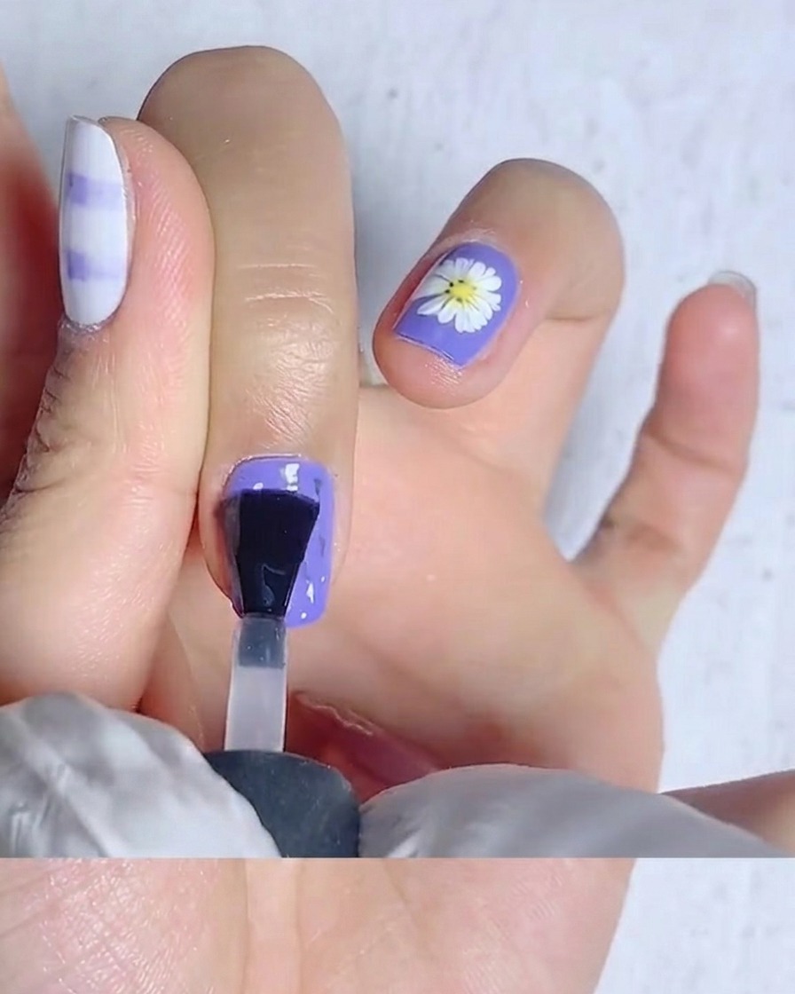 Un pincel de uñas extendiendo top coat mate sobre una uña de color amarillo brillante.