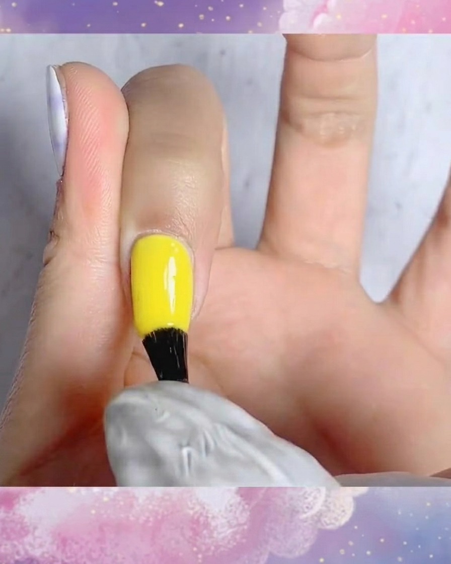 Un pincel aplicando top coat mate sobre una uña con un diseño de cuadros azul y blanco pintado a mano.