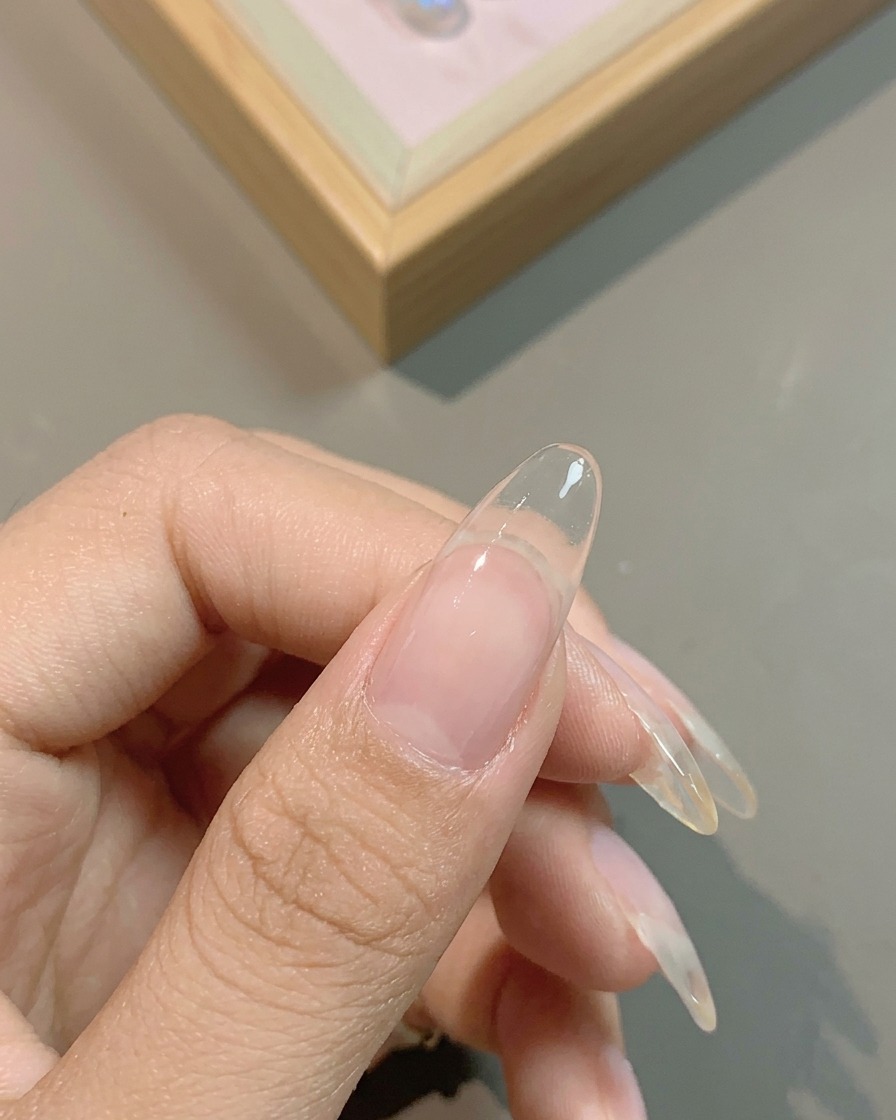 Un pincel aplicando una base de gel lechosa translúcida sobre toda la uña natural.
