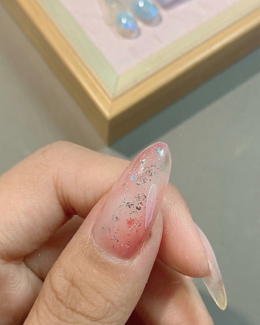 Un pincel fino trazando pétalos de margarita blancos sobre una base de gel rosa con glitter.