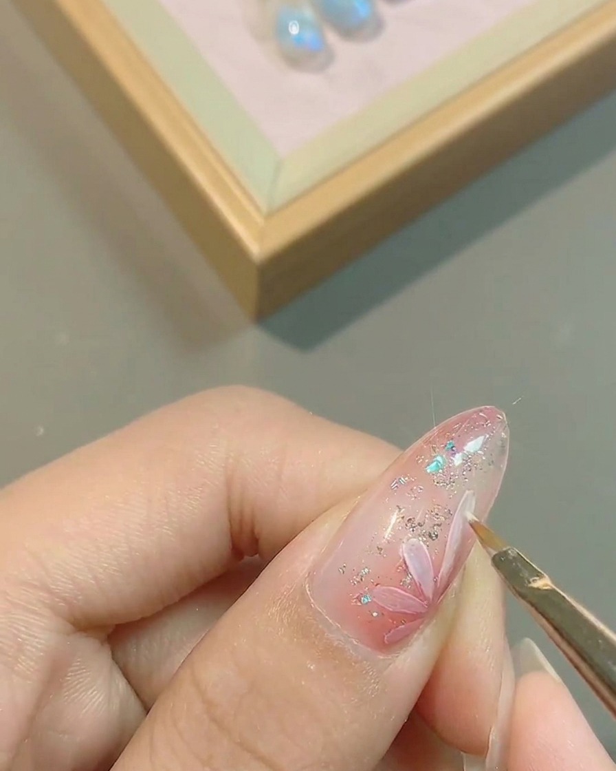Un pincel delineando con precisión los bordes de los pétalos blancos pintados sobre la uña.