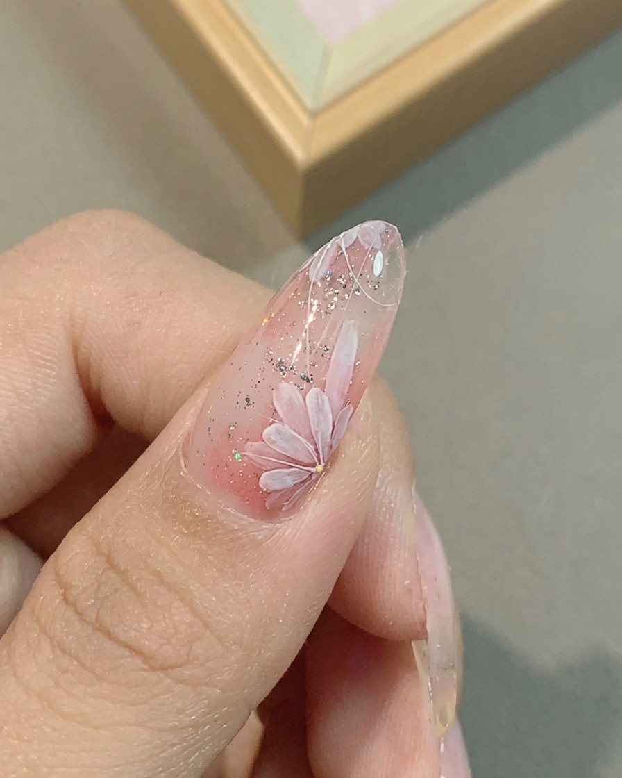 Un primer plano de una uña con pétalos de margarita siendo refinados con un pincel de detalle.
