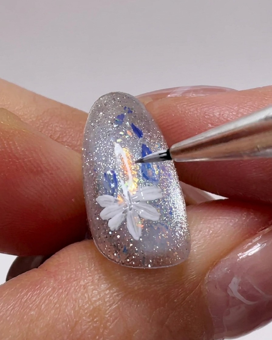 Primer plano de una uña mostrando múltiples flores de margaritas blancas siendo pintadas sobre la superficie con un pincel de detalle fino.