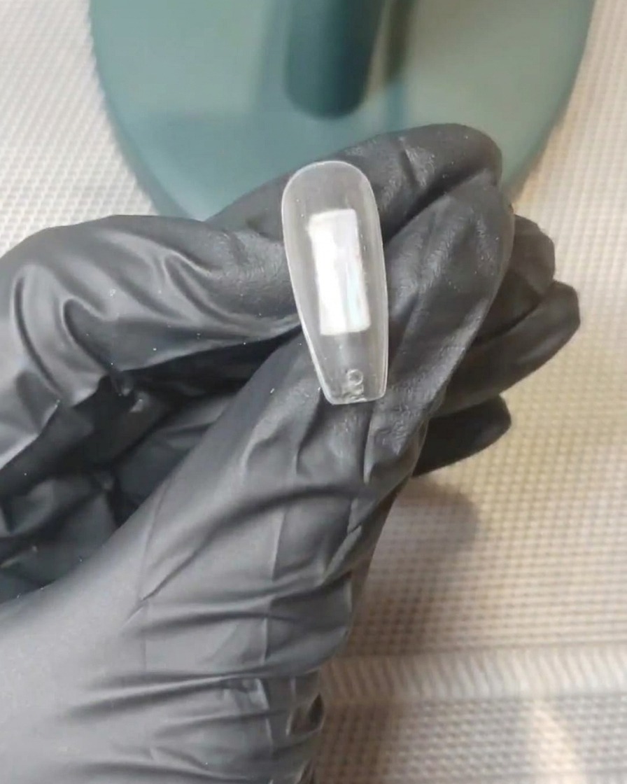 Primer plano de un tip de uña transparente con puntos distintos de gel rosa nude y blanco lechoso colocados en el centro de la superficie.