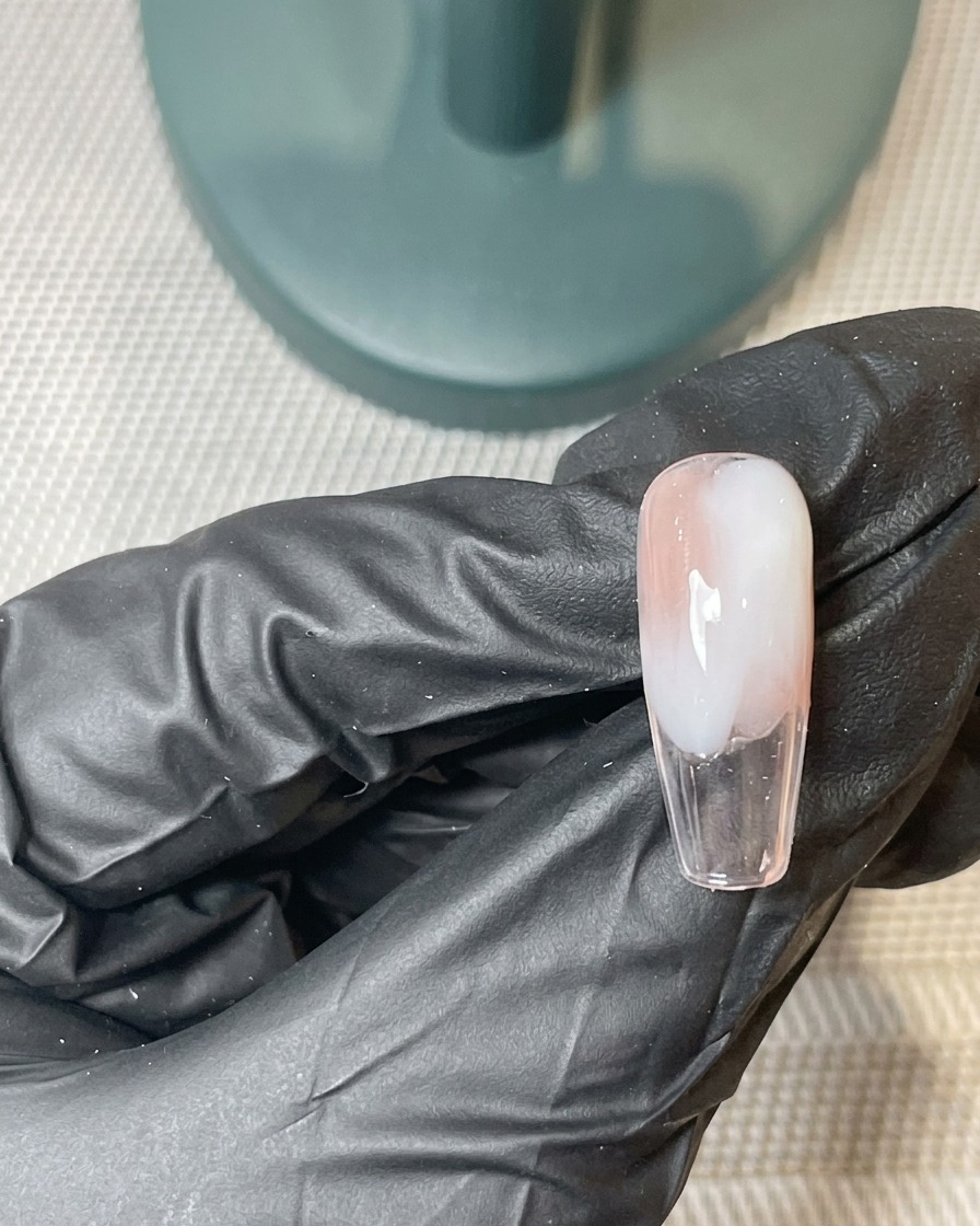 Un pincel aplicando una segunda capa fina de gel rosa y blanco sobre la base degradada previamente curada.