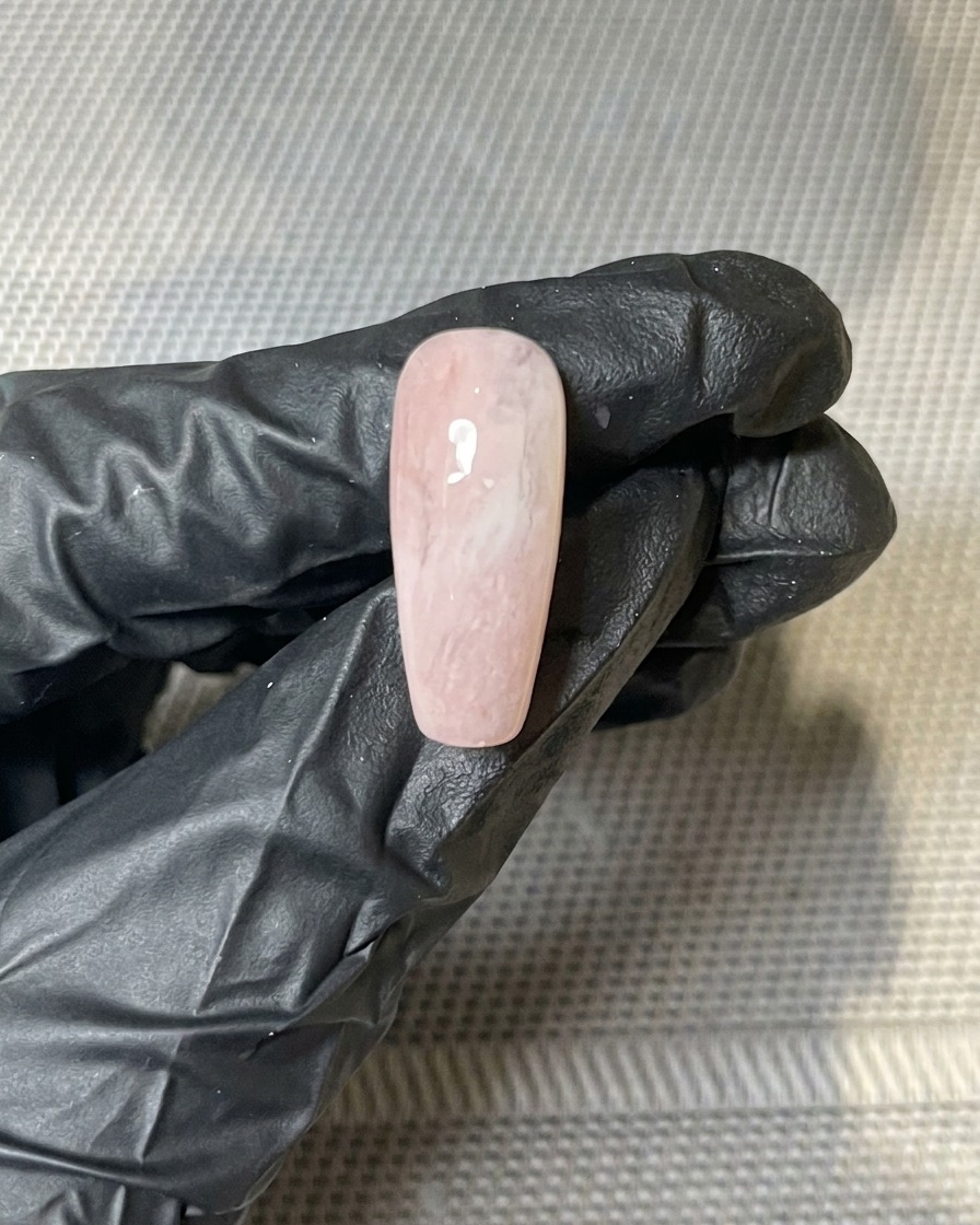 Primer plano de trozos de pan de oro presionados sobre la superficie pegajosa de una uña pintada con gel.