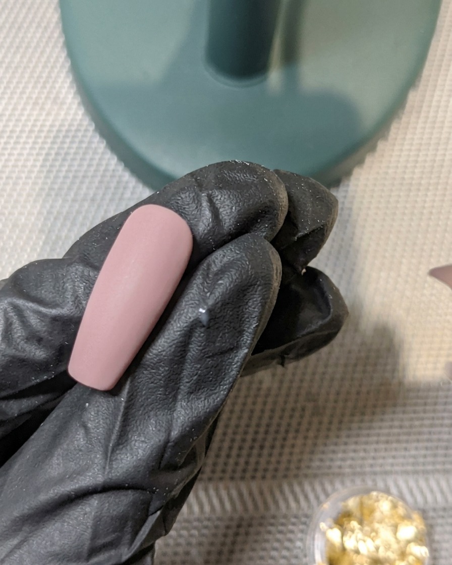 Un pincel aplicando una capa de top coat mate sobre una uña decorada con pan de oro incrustado.