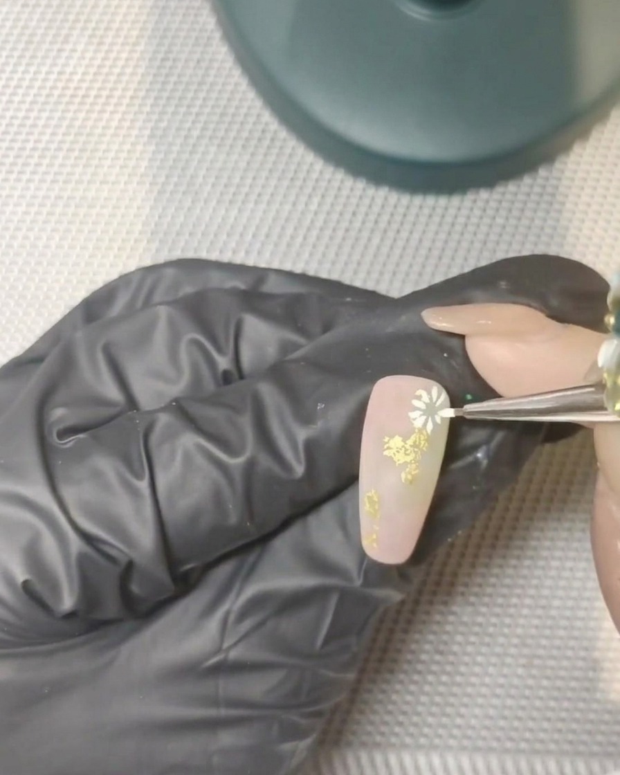 Una mano con uñas decoradas colocada dentro de una lámpara UV profesional para curar.