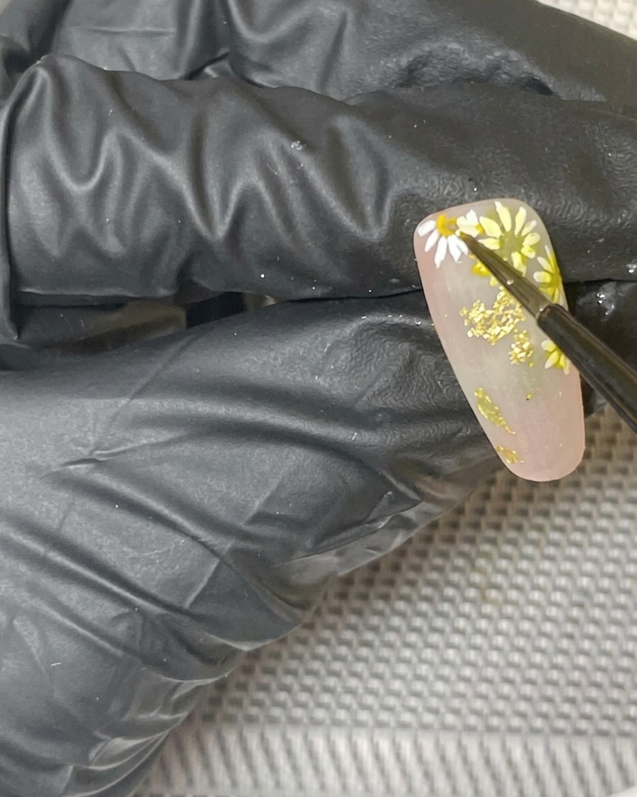 Vista en primer plano del diseño final de uñas con margaritas curándose dentro de una lámpara.