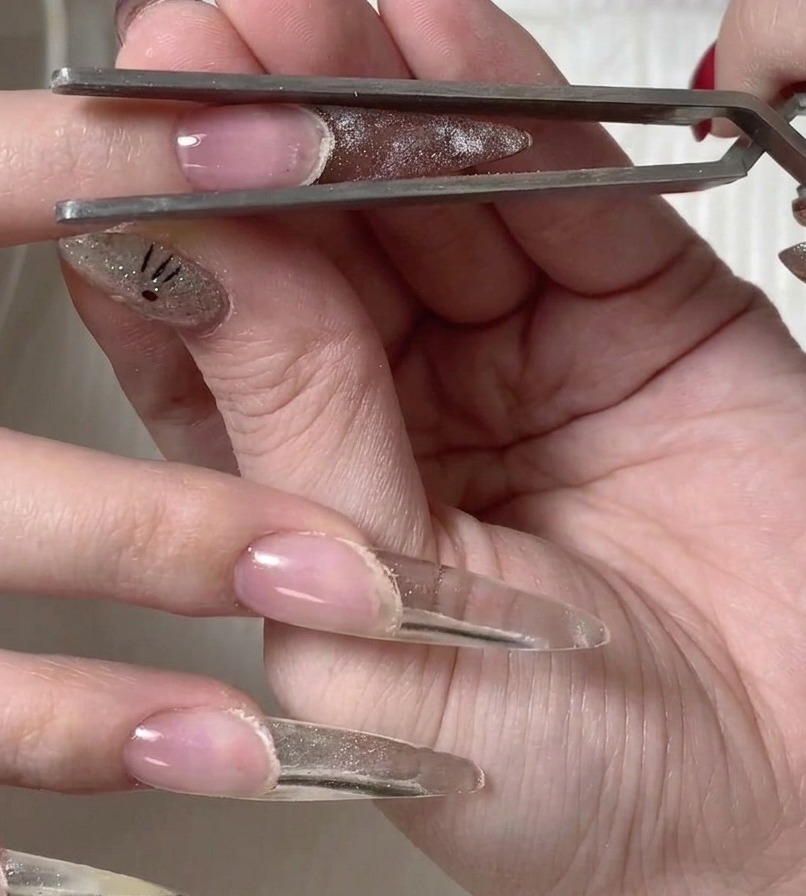 Pinzas de metal levantando con cuidado el molde de plástico de la superficie de la uña recién curada.