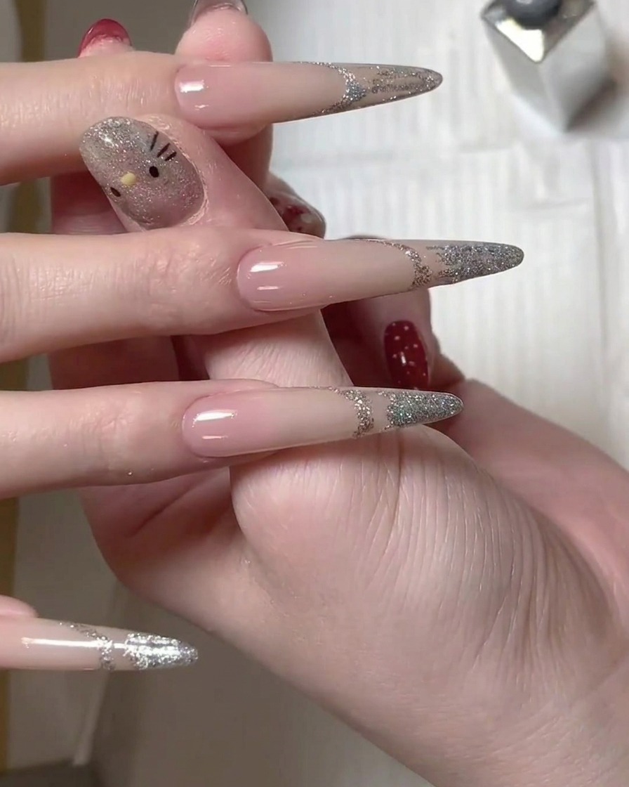 Un pincel aplicando esmalte en gel con glitter plateado en la punta de una uña larga para crear un diseño de manicura francesa.