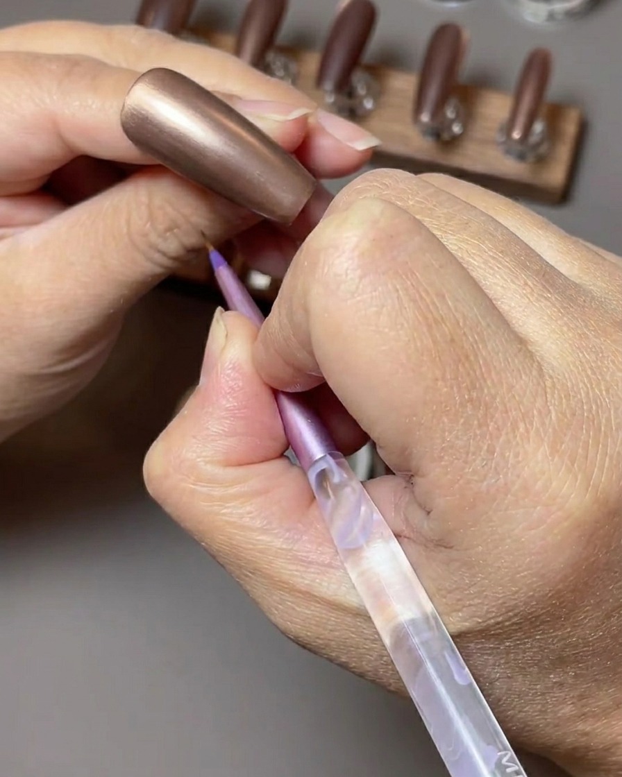 Un pincel aplicando un rico esmalte de gel ojo de gato color marrón toffee sobre una uña.