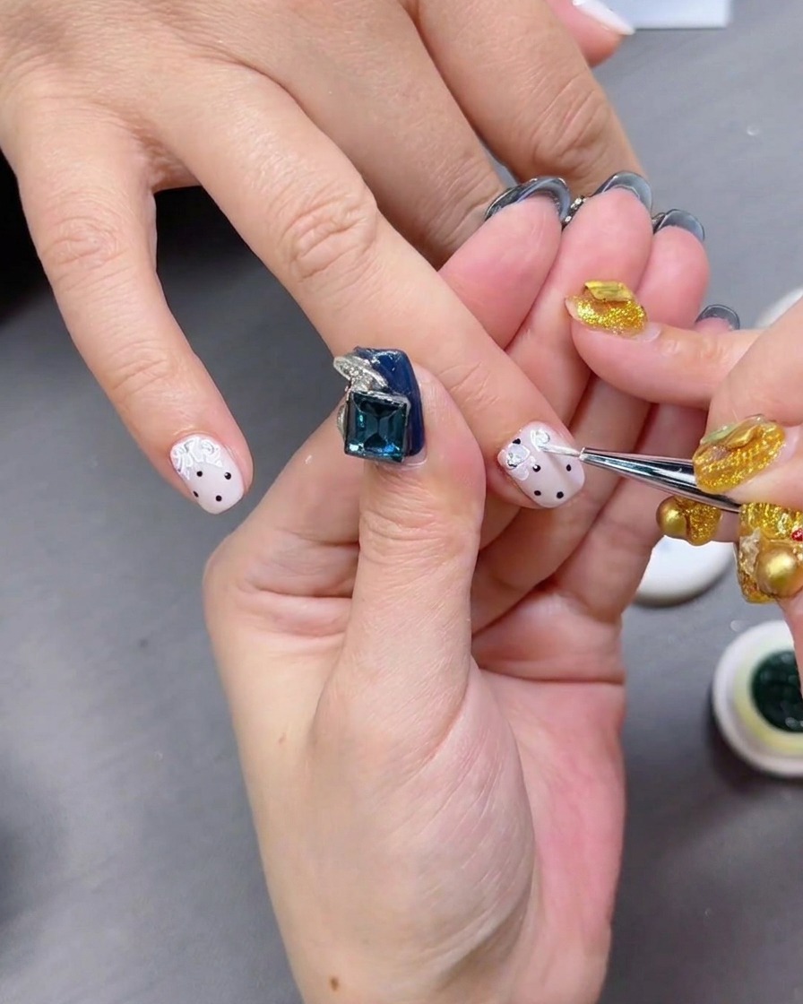 Un top coat brillante siendo aplicado sobre uñas con lunares negros.
