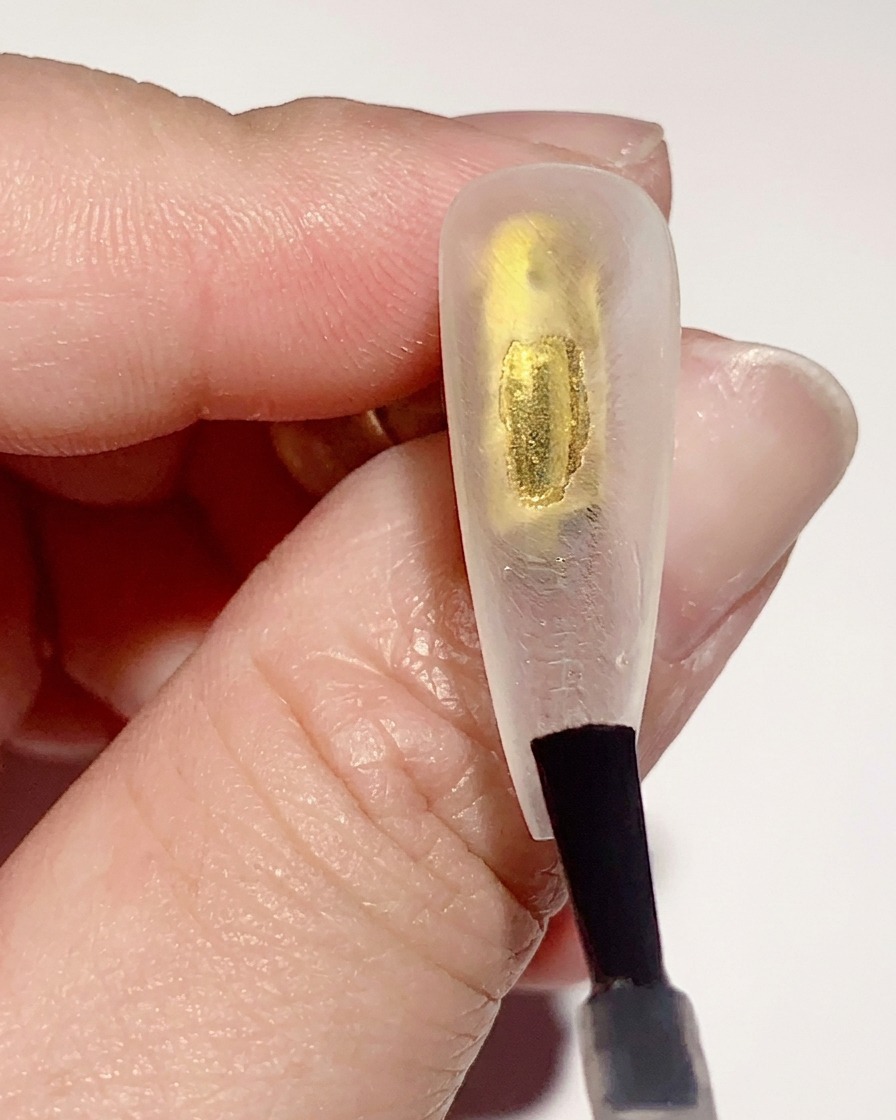 Un pincel aplicando una capa fina de base coat de gel transparente en la superficie interior de un tip transparente.