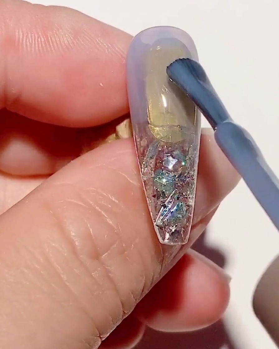 Un pincel aplicando una capa fina de esmalte de gel azul transparente sobre un tip texturizado.