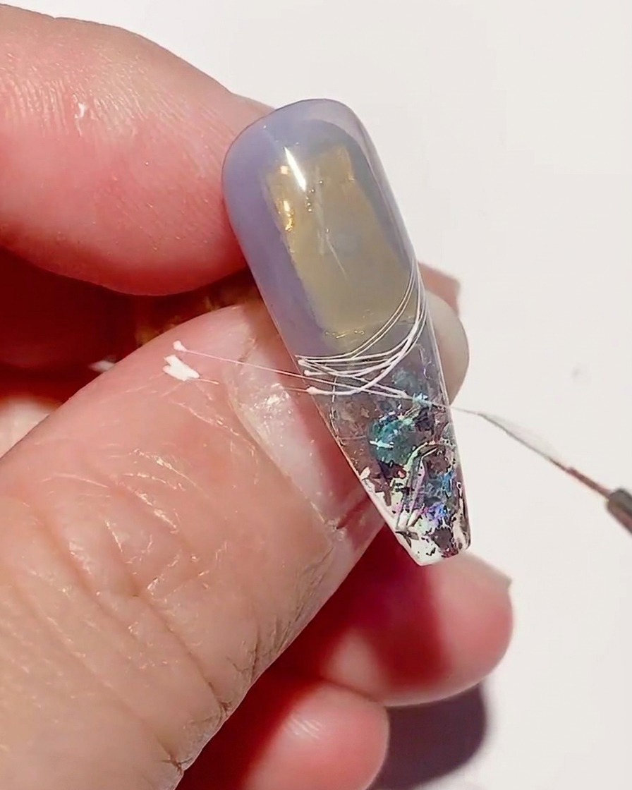 Un primer plano de una uña con líneas de spider gel blanco siendo curadas bajo una lámpara de uñas UV.