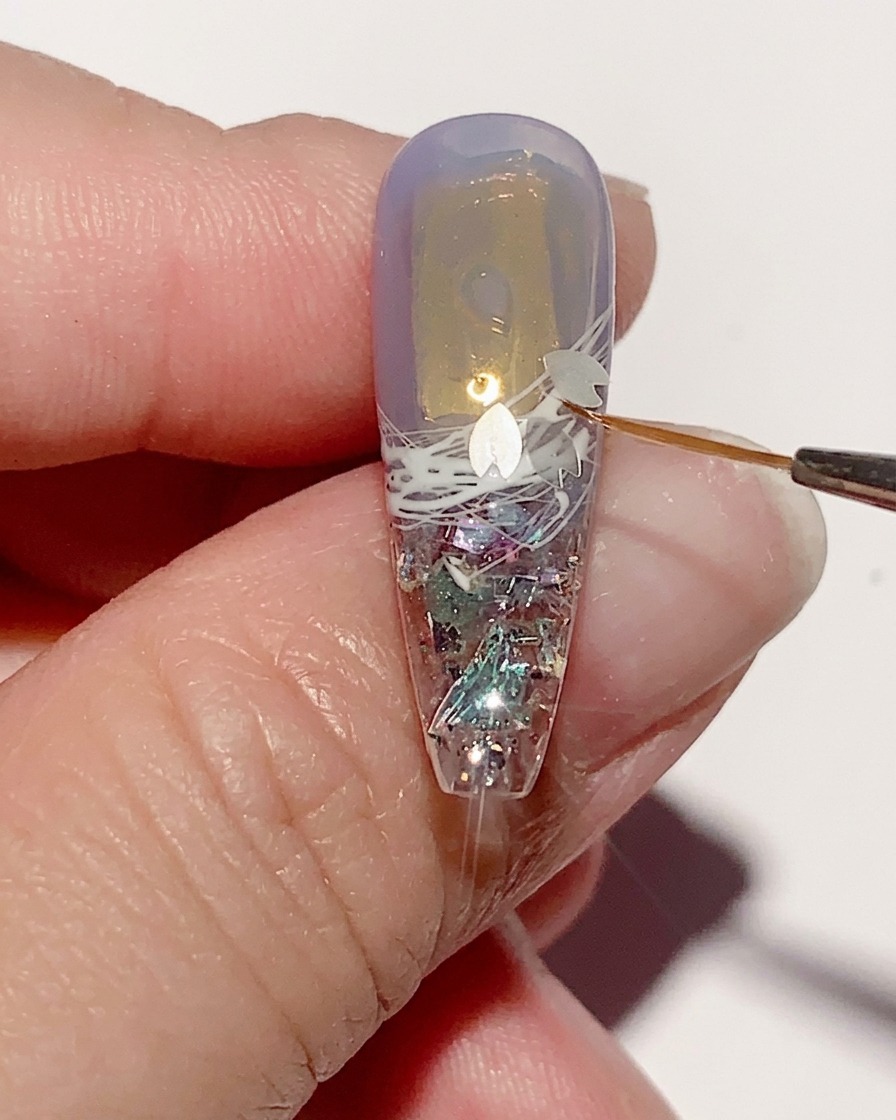 Pinzas colocando pequeñas y delicadas lentejuelas con forma de flor de cerezo sobre la superficie de gel húmeda de una uña.