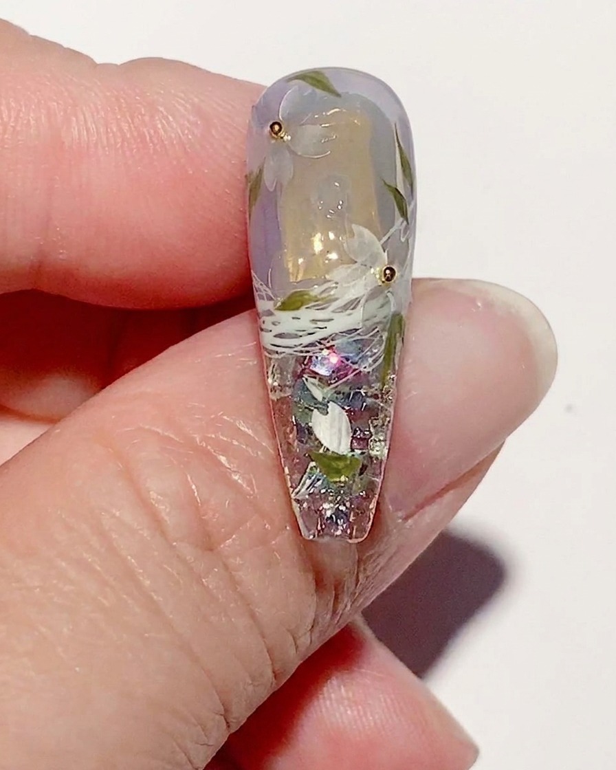 Una uña manicurada con arte de flores de cerezo, mostrando la aplicación de un top coat brillante sobre todo el diseño.