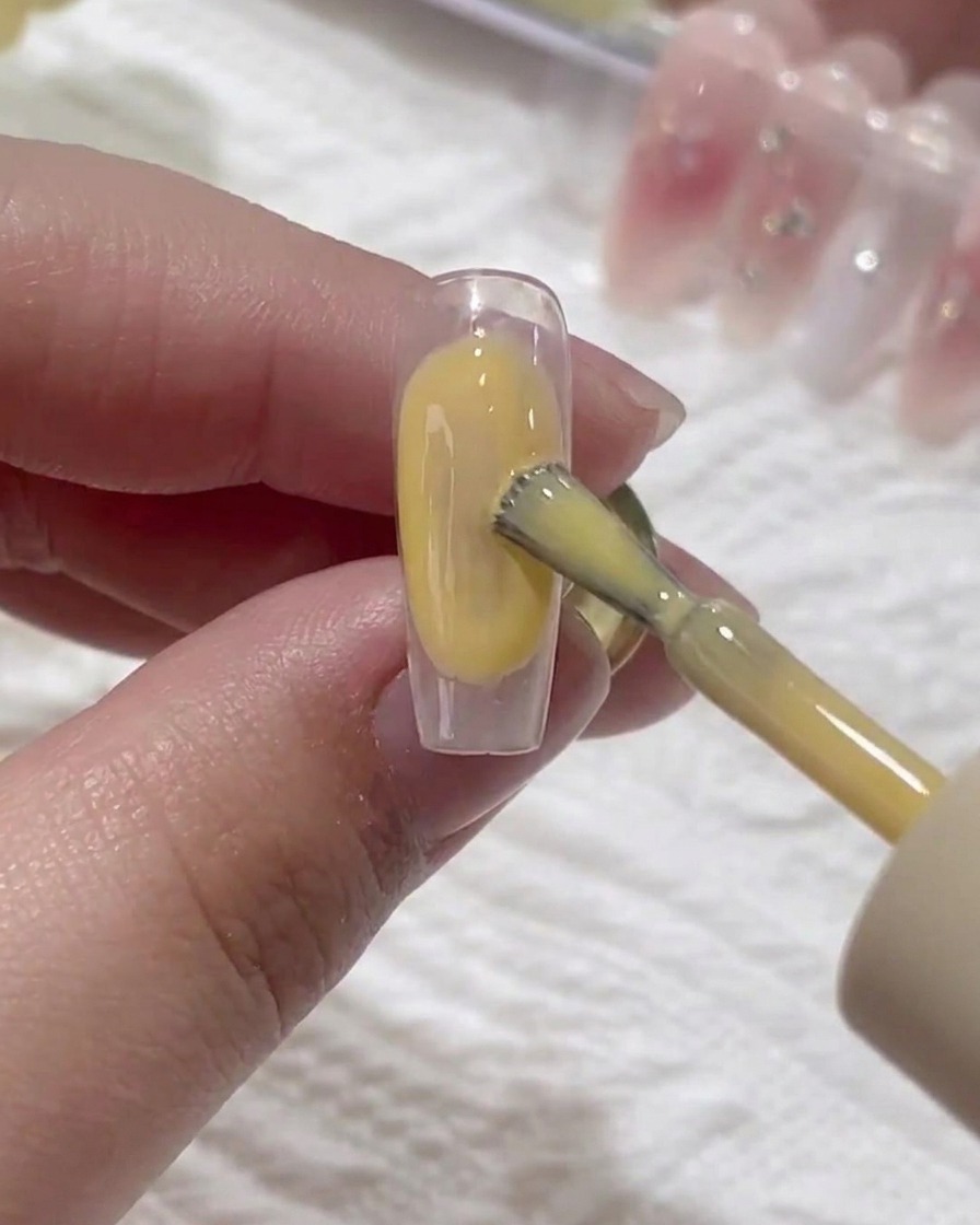 Un pincel aplicando una capa fina de gel base transparente sobre una uña natural.