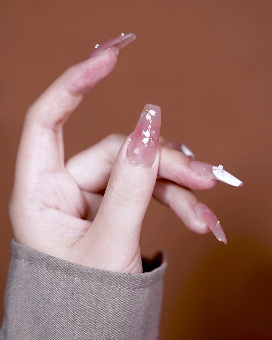 Un pincel aplicando un gel adhesivo espeso y transparente sobre una uña con base de degradado rosa.