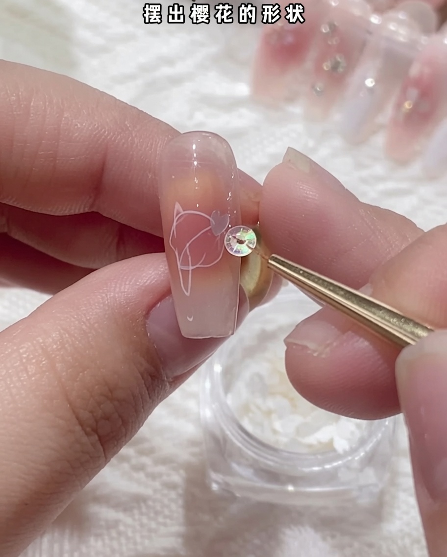 Primer plano de unas pinzas sosteniendo una delicada lentejuela blanca de flor de cerezo y colocándola sobre la superficie de la uña.