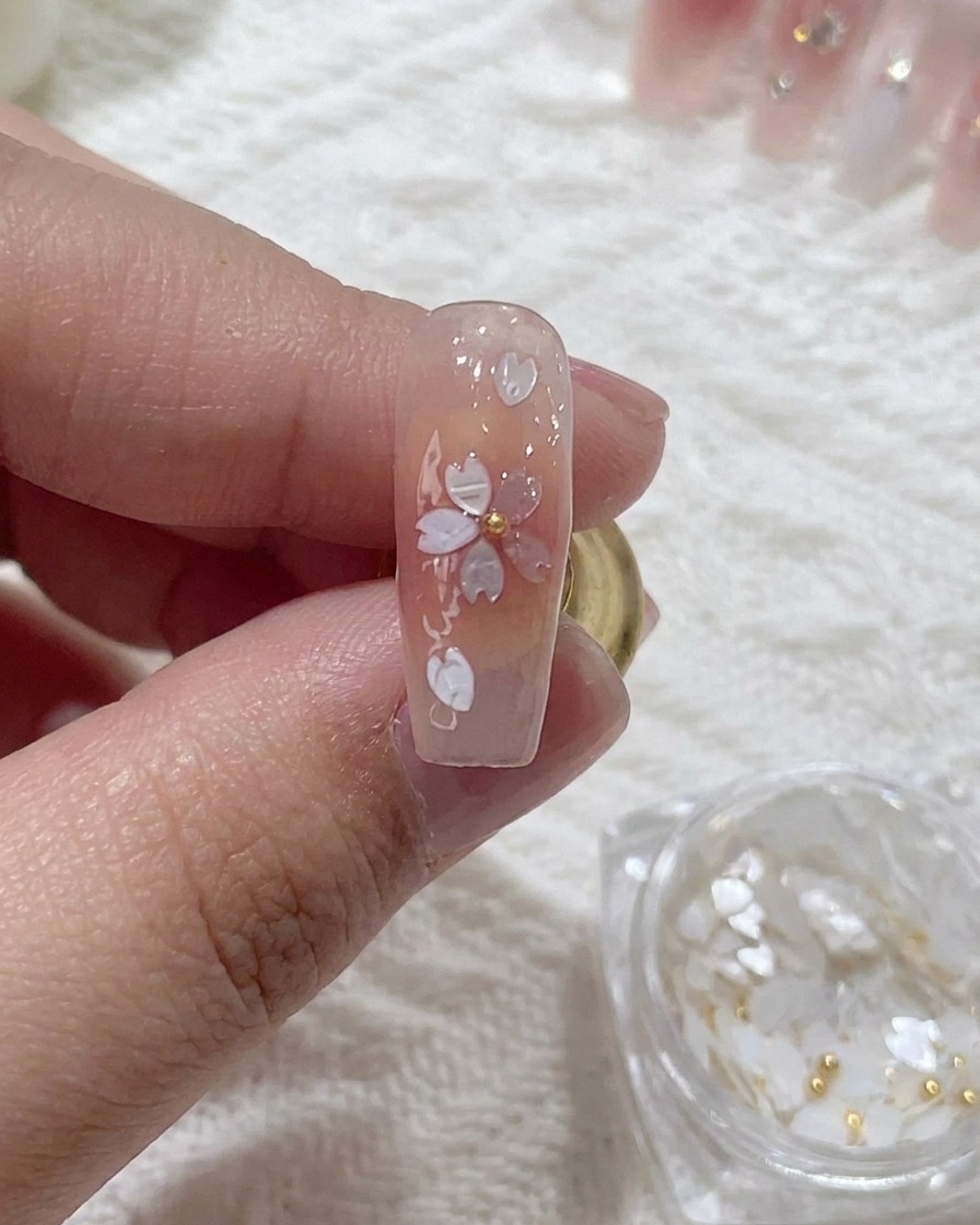 Primer plano de una cuenta metálica siendo presionada en el centro de un diseño de uña de flor de cerezo.
