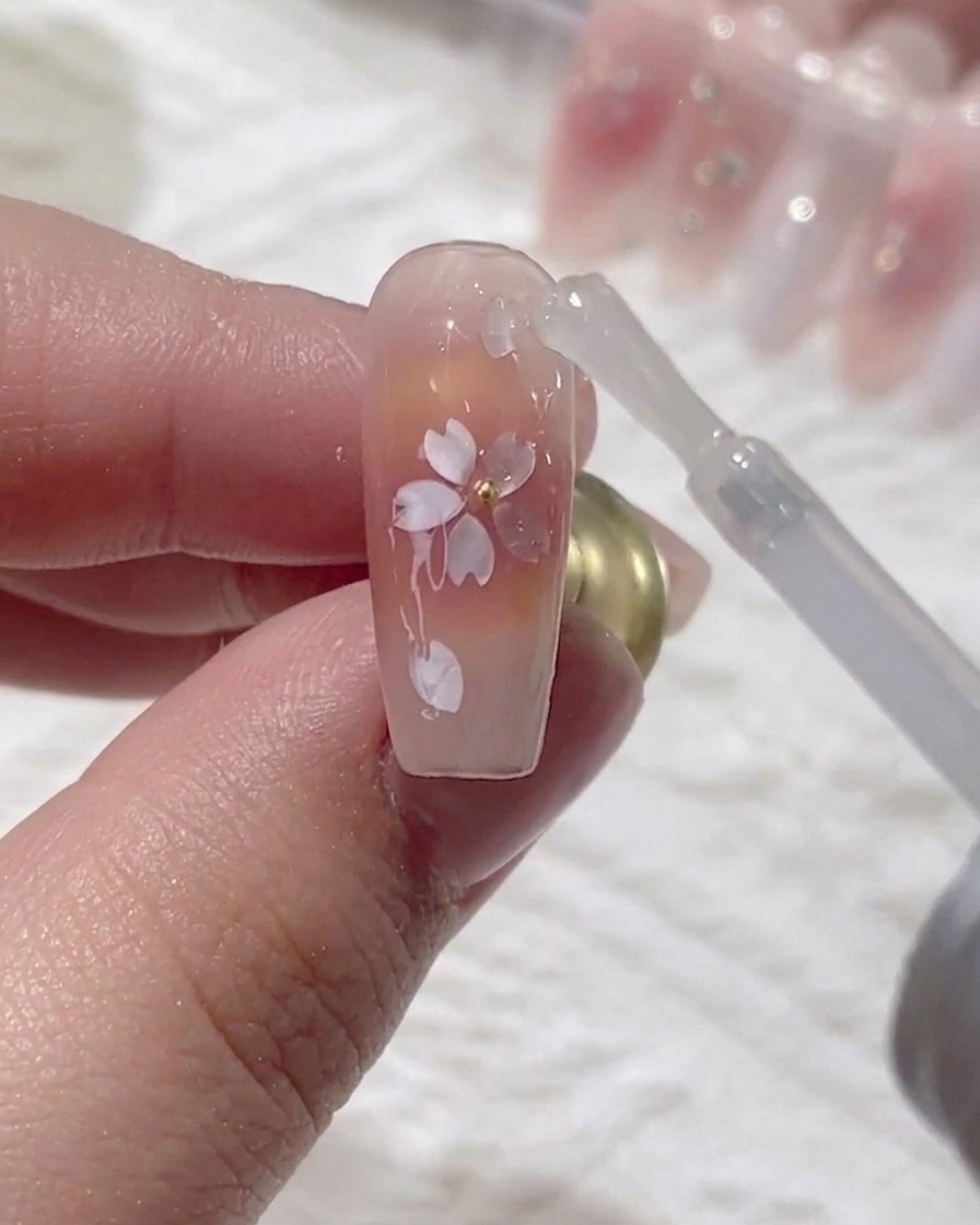 Un pincel aplicando una capa final de top coat de alto brillo sobre el diseño de flor de cerezo encapsulado.