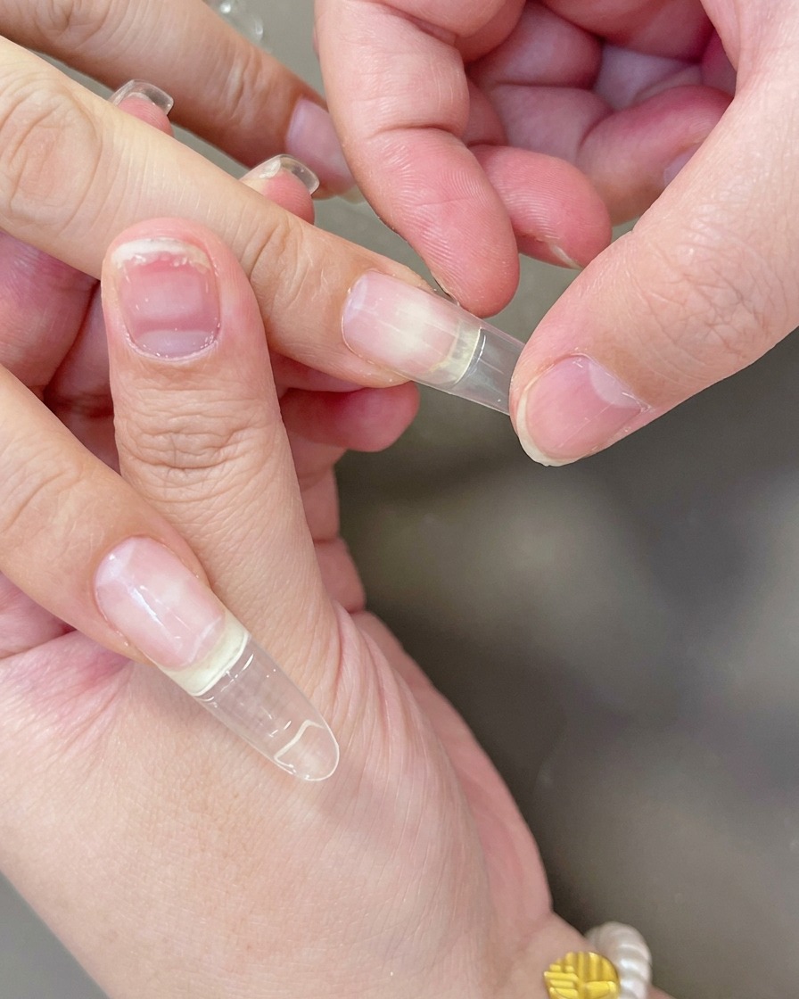 Dedos presionando un tip de gel transparente sobre la uña para asegurar su correcta adherencia.