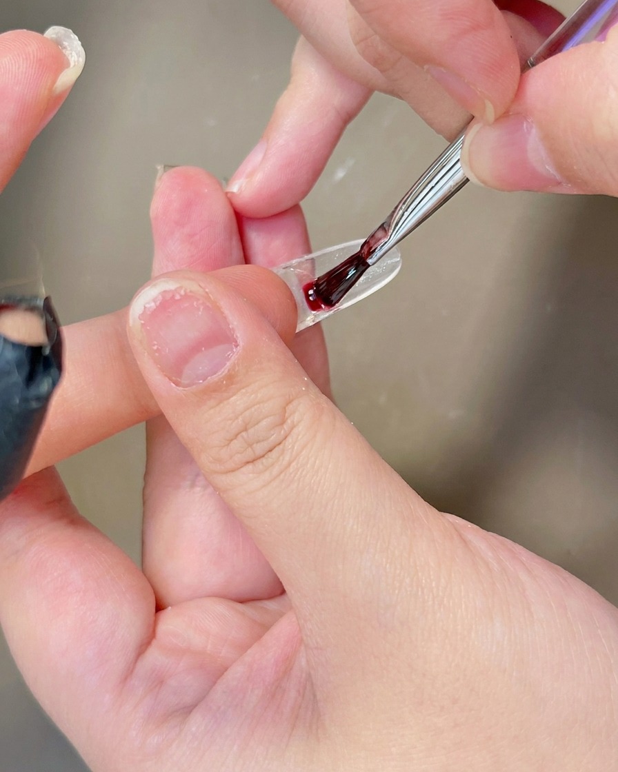 Un pincel aplicando una capa de esmalte de gel blanco lechoso y translúcido sobre la superficie de un tip.