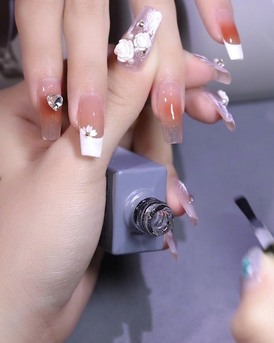 Pinzas colocando una pequeña lentejuela con forma de flor de cerezo blanca sobre la superficie de la uña.