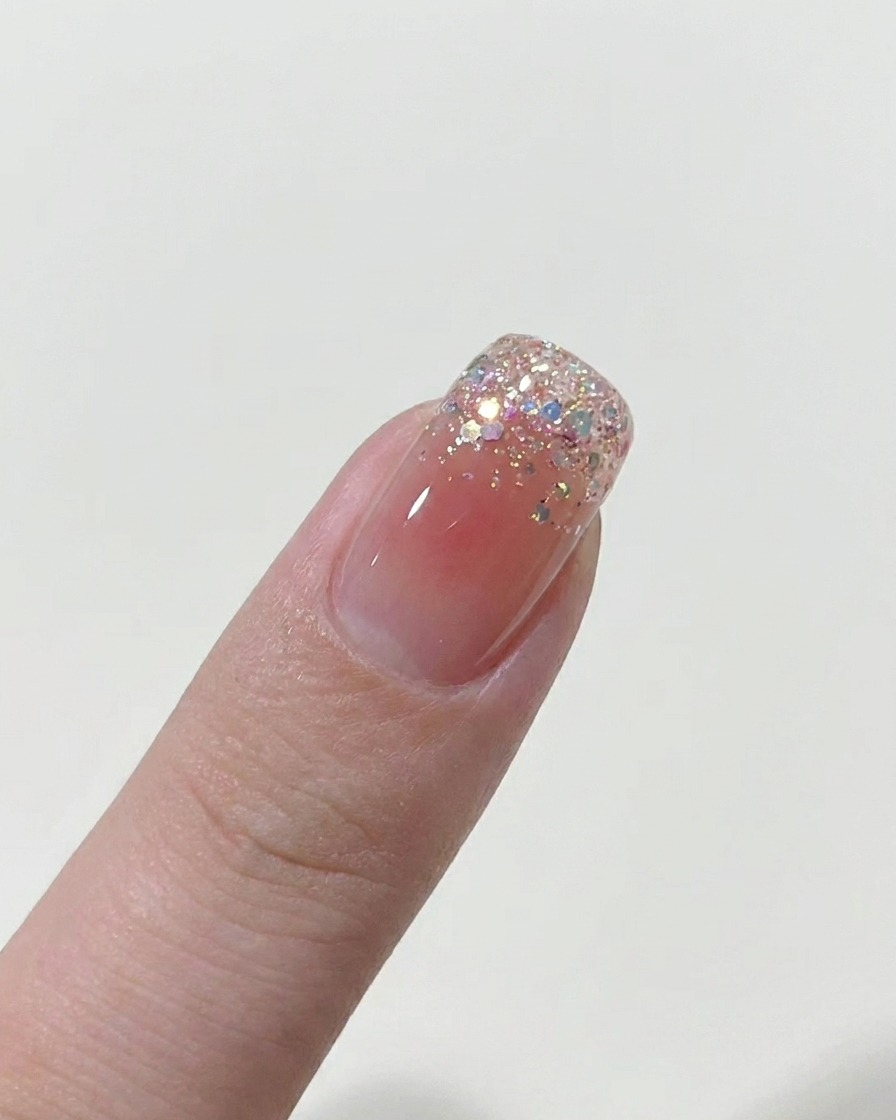 Un pincel aplicando una capa fina de esmalte de gel nude sobre una uña desnuda.