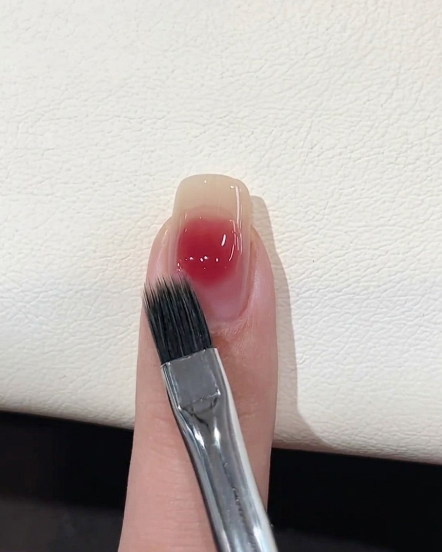 Un pincel plano de difuminado suavizando los bordes de un punto de gel rosa sobre una uña.