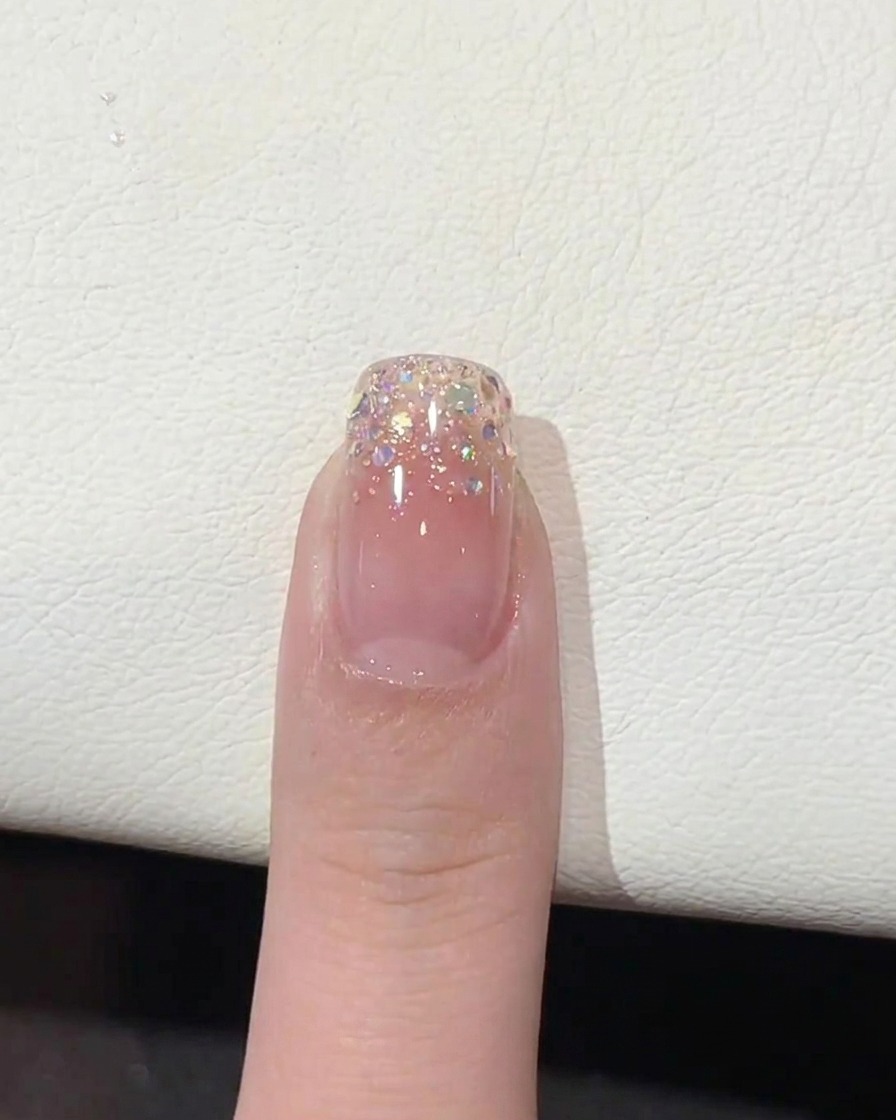 Un pincel aplicando un top coat transparente y brillante sobre la punta con degradado de brillo.