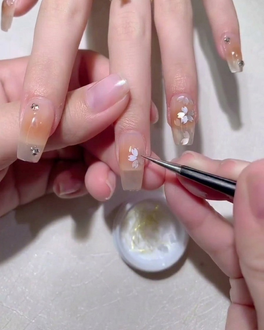 Pinzas colocando una lentejuela de pétalo de sakura sobre la superficie de la uña con gel húmedo.