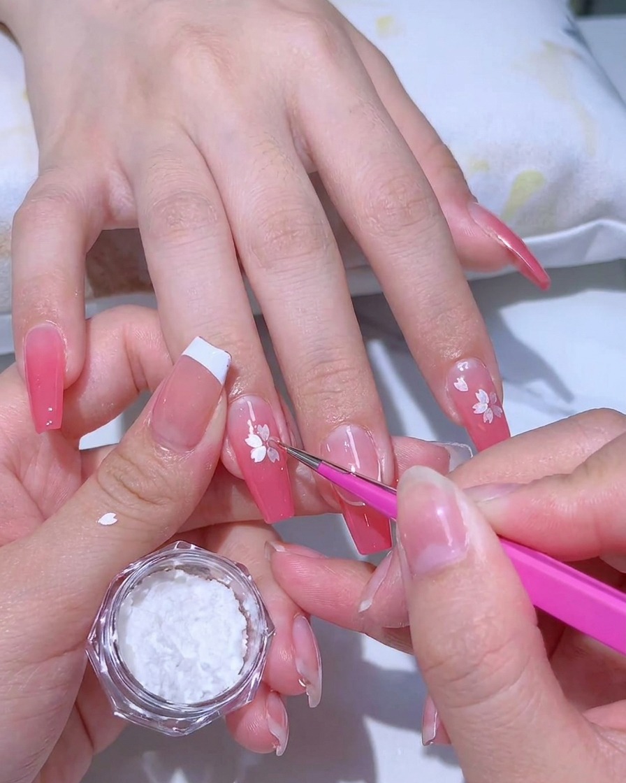 Aplicación de un gel adhesivo transparente sobre una manicura con degradado rosa usando un pincel de punta fina.