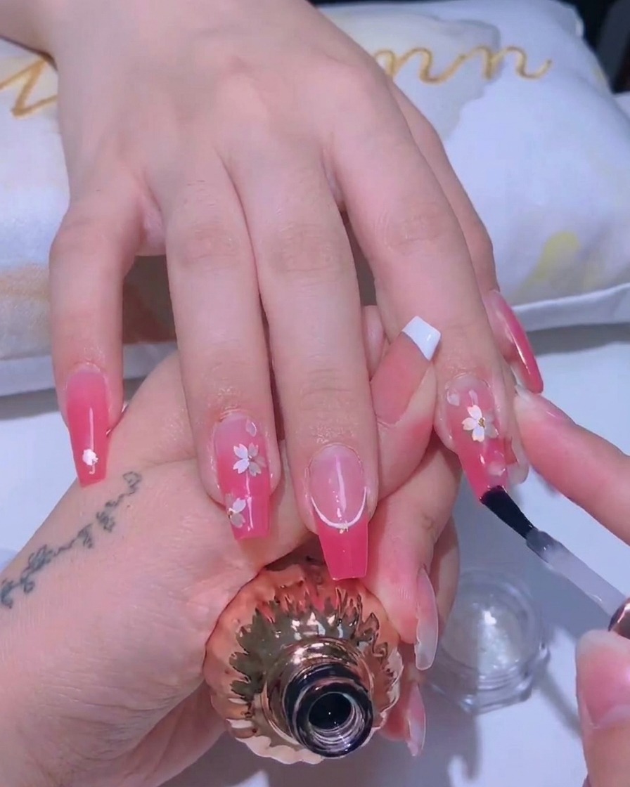 Un pincel aplicando un top coat brillante sobre un diseño de uñas de flores de cerezo.