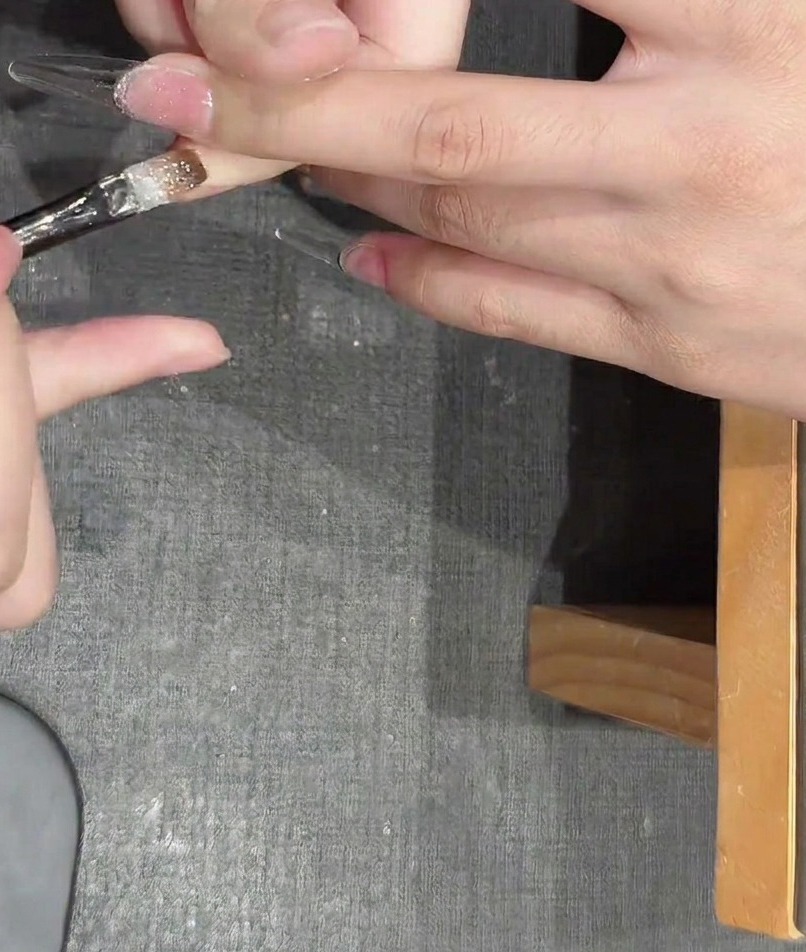 Pinzas colocando pequeñas piezas de glitter metálico en forma de estrella sobre una uña con gel húmedo.