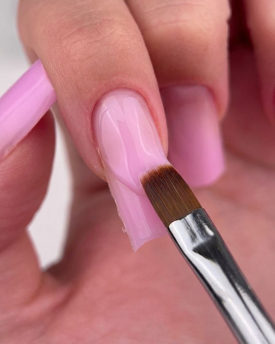 Un pincel delineador fino limpiando cuidadosamente el borde del gel rosa en la cutícula.