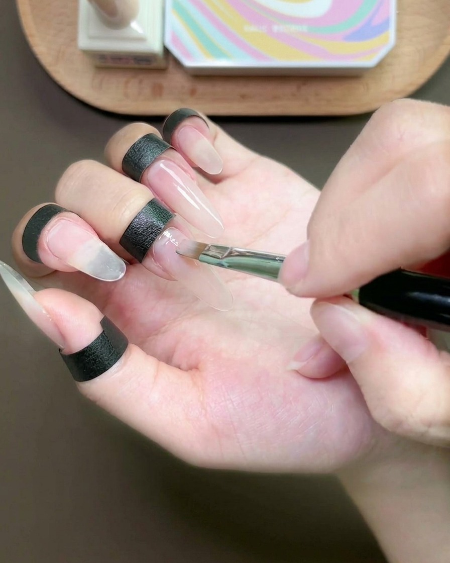 Un pincel plano aplicando una fina capa de gel nude sobre la uña del dedo medio.