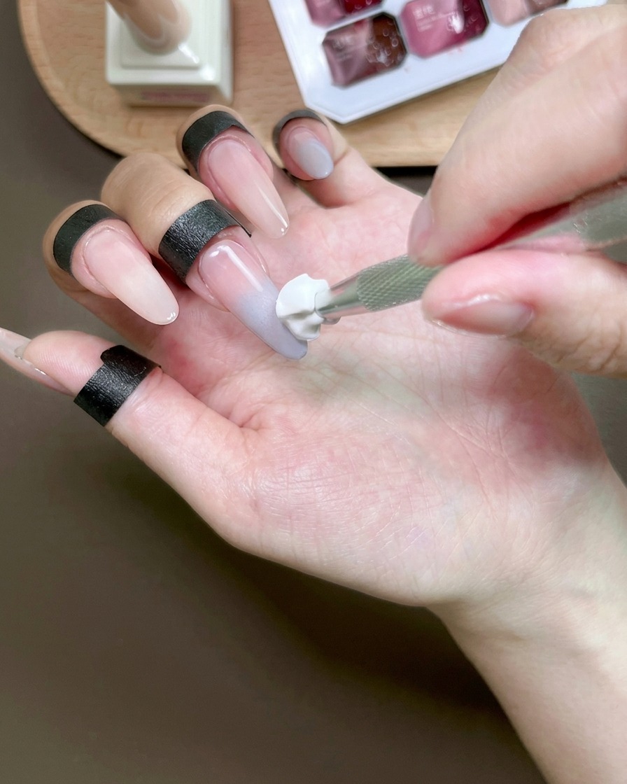 Una esponja difuminando gel azul en una uña para crear un efecto ombré.