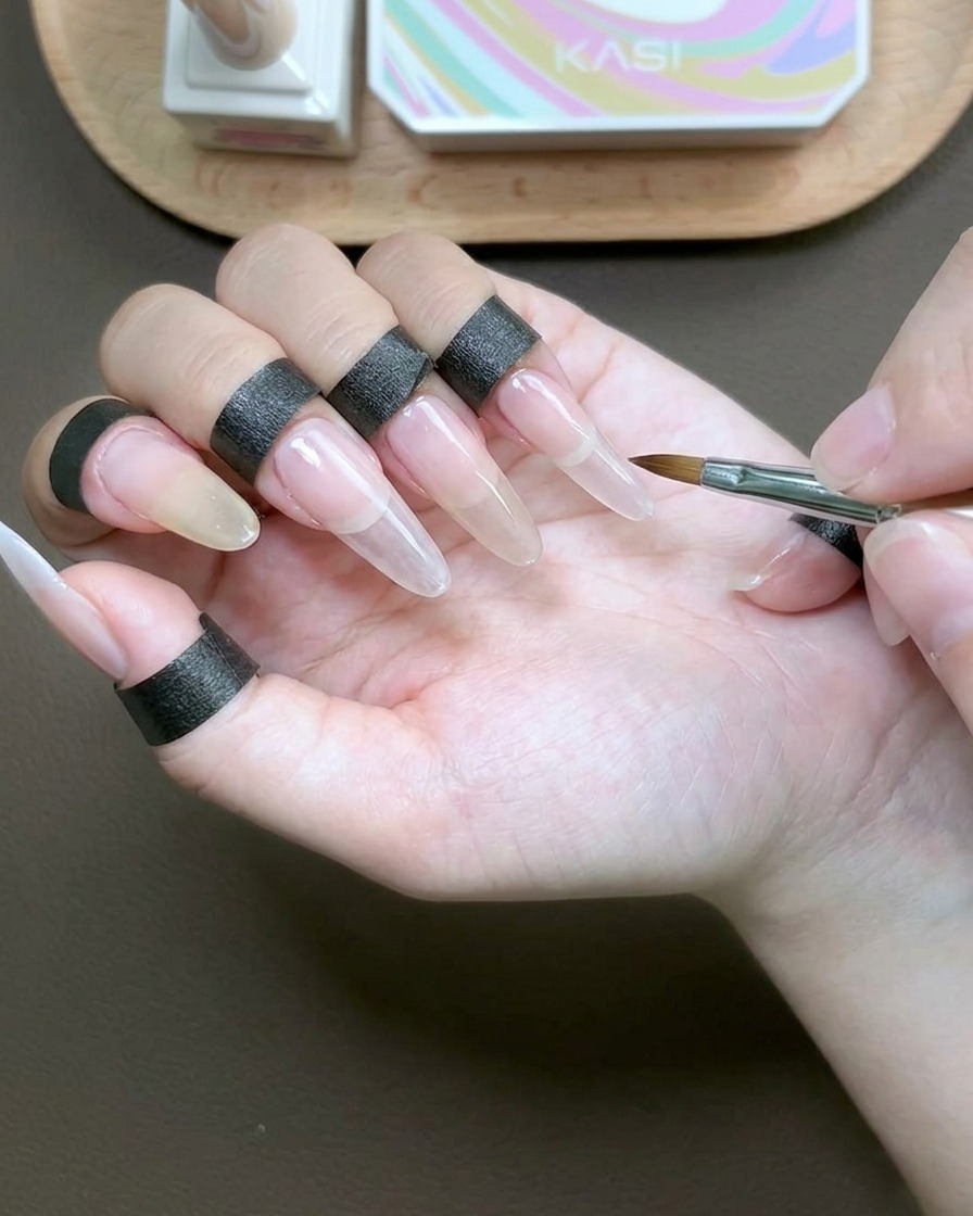 Un pincel aplicando un gel constructor transparente y viscoso sobre toda la superficie de la uña del dedo índice para su encapsulación.
