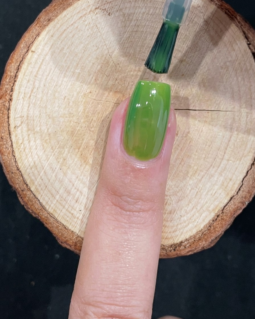 Un pincel aplicando meticulosamente esmalte de gel verde cerca de la cutícula de una uña.
