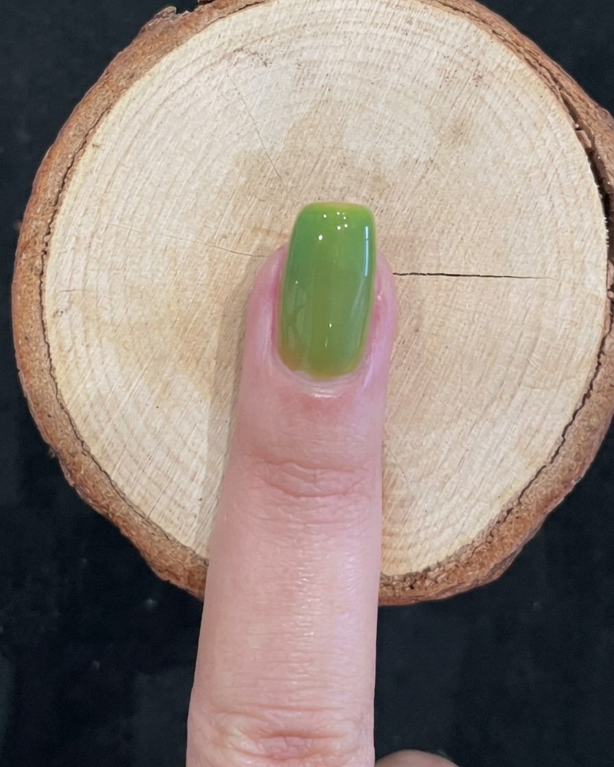 Una uña curada con un acabado verde translúcido, limpio y brillante sobre una superficie de madera.