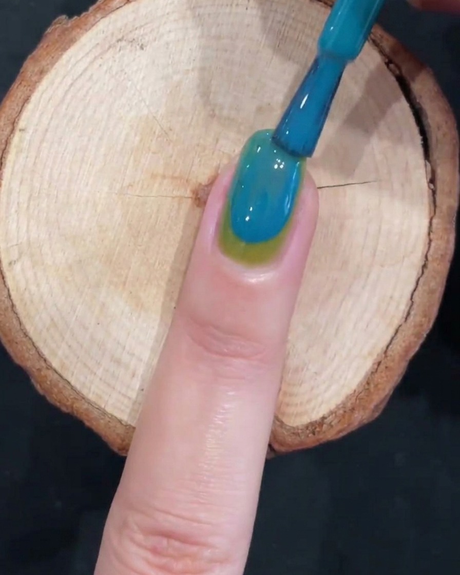 Un pincel creando un efecto de gradiente suave en una uña de dos tonos, verde y azul.