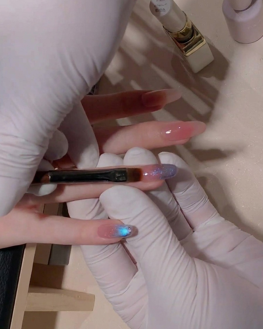 Un primer plano que muestra un pincel plano de gel difuminando suavemente el área de transición del gel cat-eye azul sobre la superficie de la uña.