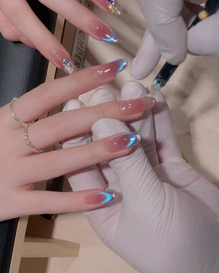 Una vista en primer plano de un pincel de uñas mezclando esmalte de gel de tonos azules en una uña para crear un efecto degradado suave y fluido.
