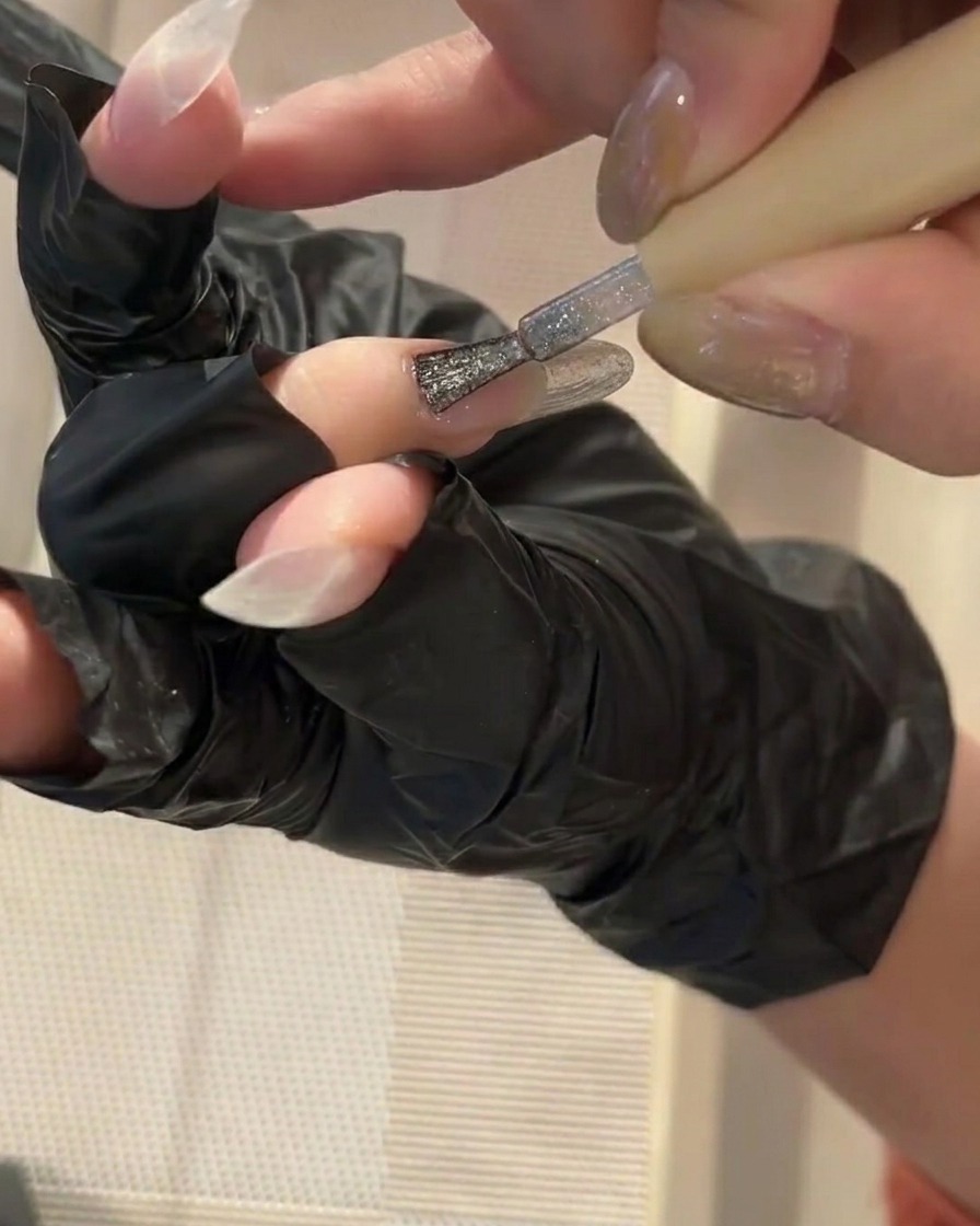 Un pincel pequeño aplicando una capa fina de base coat transparente en una uña limpia.