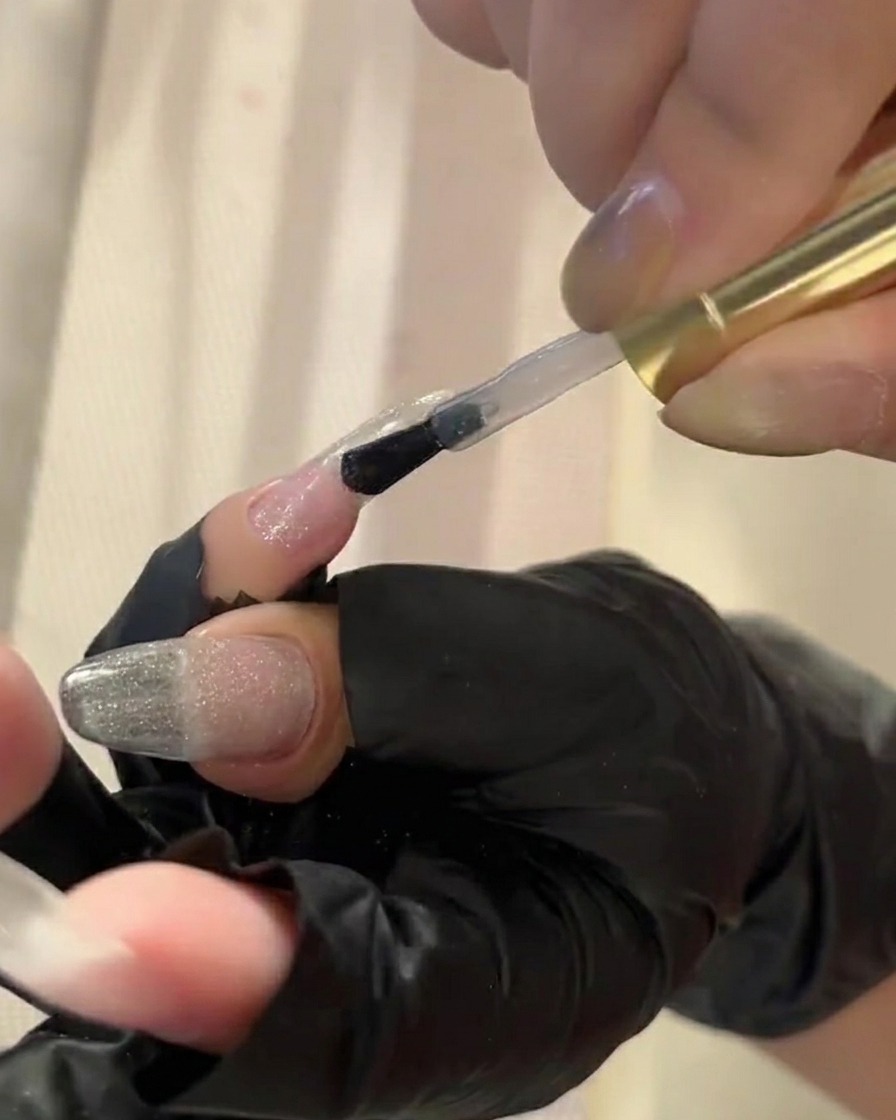 Un pincel aplicando top coat transparente a una uña para preparar la aplicación de pigmento.
