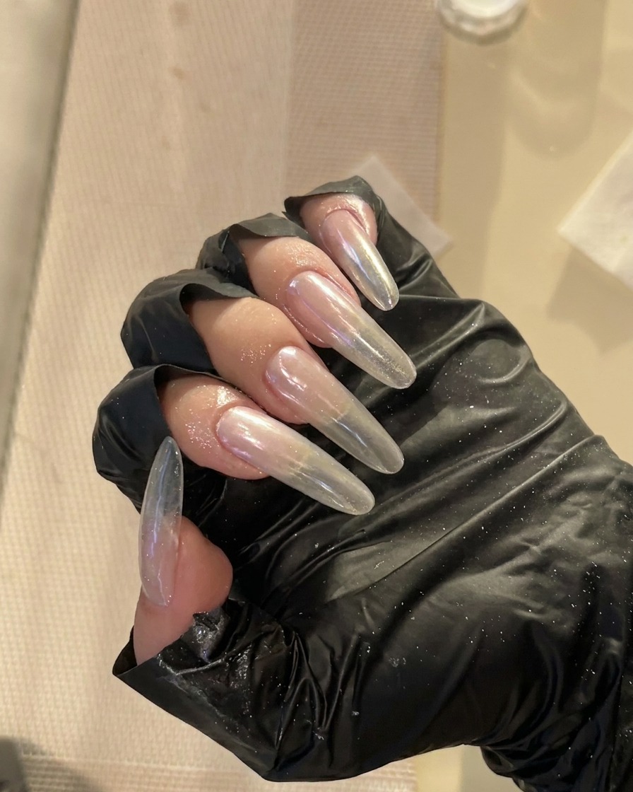 Primer plano de uñas largas almendradas siendo refinadas en los laterales con una lima profesional.