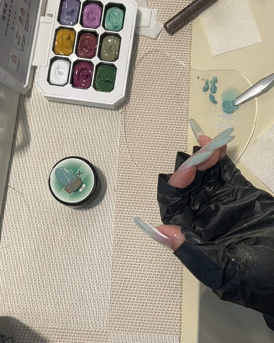 Pincel aplicando top coat brillante en una uña con diseño degradado verde menta.